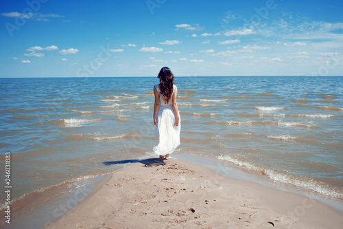 Young beautiful brunette woman in white dress on the seashore.