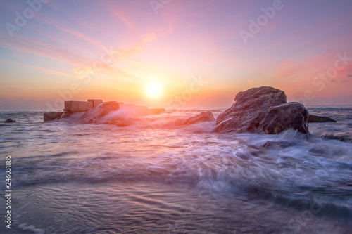 Bright colorful sunrise on the beach. Sea waves in the bright rays of the sun