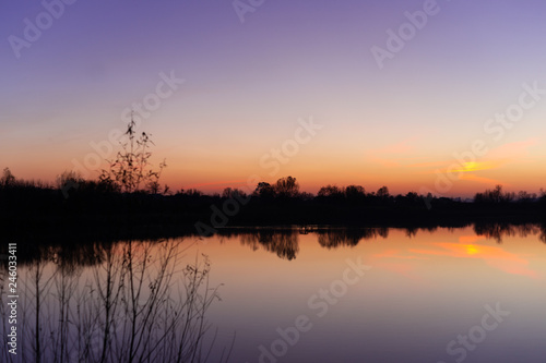 Blue time evening sky landscape with trees and lake in foreground. Blue time sunset. Perfect teal and orange colors. Low-light underexposed photo.