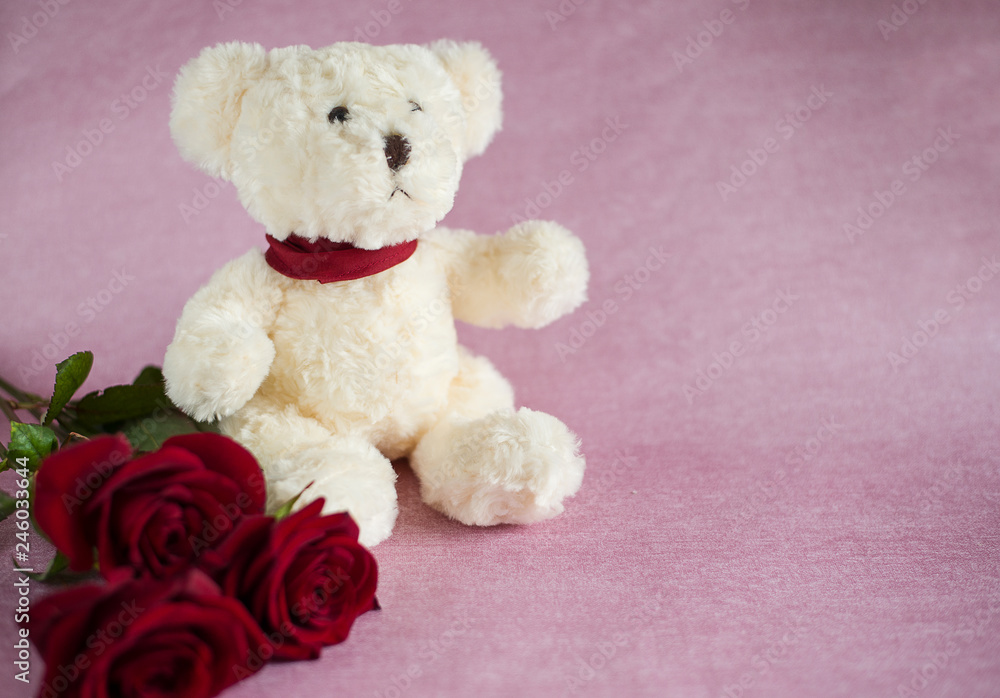 a white toy bear and three red roses lie on a pink background (horizontally, close up)