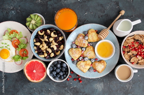 Brunch or breakfast concept on dark background. Healthy breakfast fried egg, salad, pancakes, juice, coffee, granola and dried fruits. Top view with copy space. Valentine's Day or Mather's Day concept