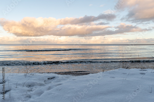 A beautiful cloudy day on the snowly coast. The low winter sun shines through the clouds.