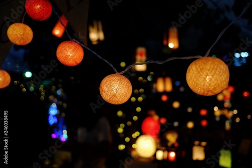 Fototapeta Naklejka Na Ścianę i Meble -  A colorful ball bulbs hanging on a wire and glowing in the dark night with plenty yellow bokeh background 
