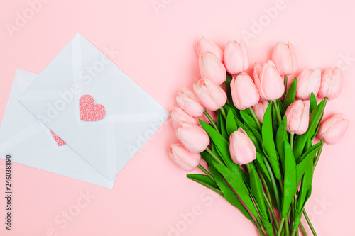 Fototapeta Naklejka Na Ścianę i Meble -  Female hands with a bouquet of pink tulips and blank white letter envelopes, on a pink background. View from above.