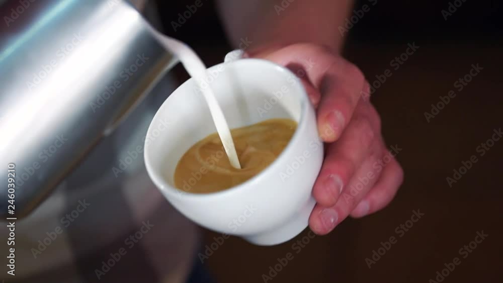 Barista pouring latte foam over coffee making a perfect cappuccino and creating a white heart. White cup with cappuccino Barista pouring latte foam over coffee making a perfect cappuccino and creating a white heart. White cup with cappuccino