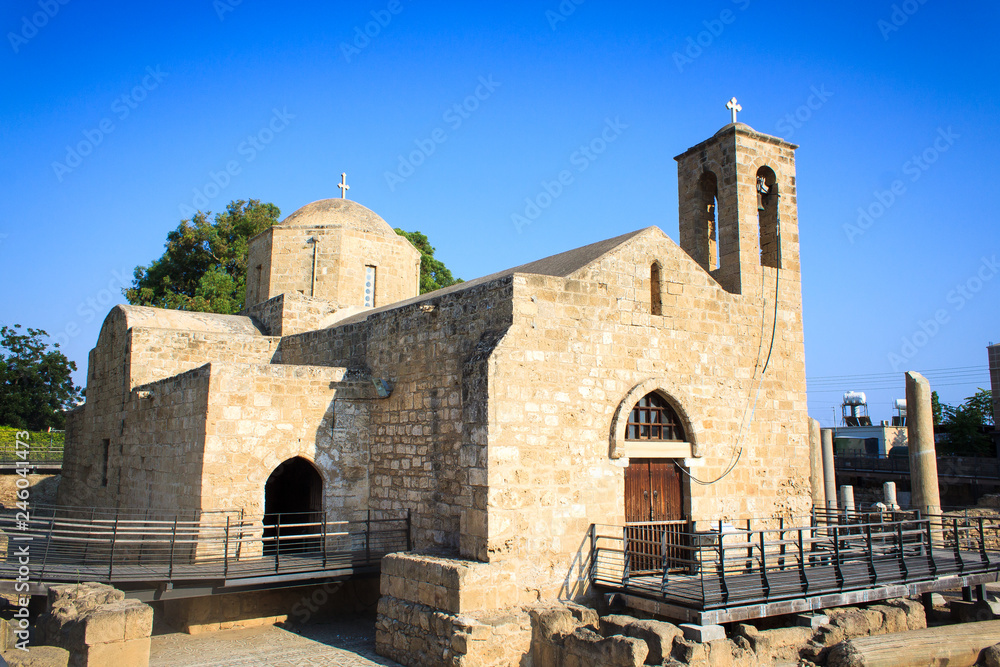 A large white church with a bell tower in ancient ruins in the midst of ancient columns on the island of Cyprus