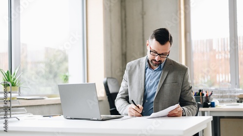 Middle aged handsome businessman in shirt working on laptop computer in office
