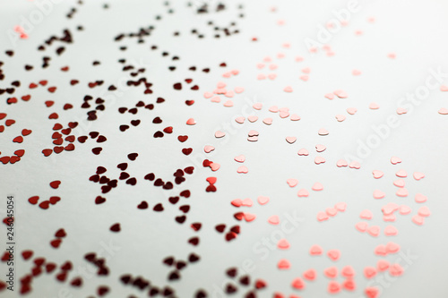  Small red sparkling hearts are scattered on a white background in soft focus. A good shot for an article about love and Valentine s Day or wedding
