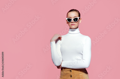 Fashion studio image of gorgeous elegant woman in white knitted golf and sunglasses posing over pink wall.