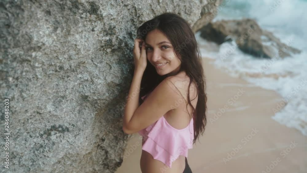 Close-up portrait of smiling beautiful girl, posing near the rock on the beach with big waves. Slow-motion Close-up portrait of smiling beautiful girl, posing near the rock on the beach with big waves. Slow-motion