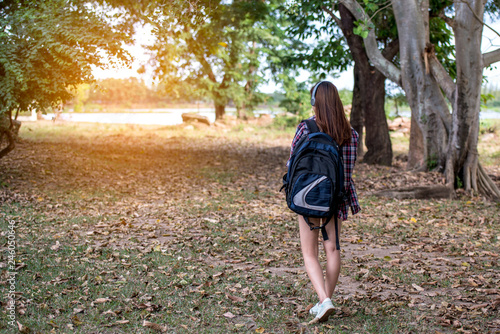 A beautiful young woman with headphones carrying a bag walking in the park.
