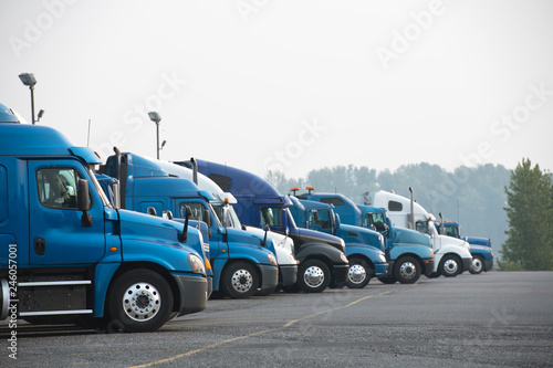 Profiles of different big rigs semi trucks standing in row on parking lot