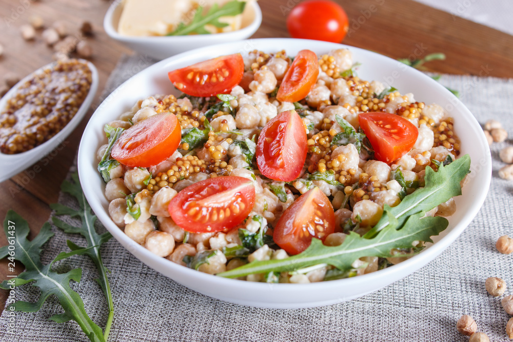 Vegetarian salad of boiled chickpeas, cheese, arugula, mustard and cherry tomatoes on brown wooden background. Vegetarian salad of boiled chickpeas, cheese, arugula, mustard and cherry tomatoes on brown wooden background.