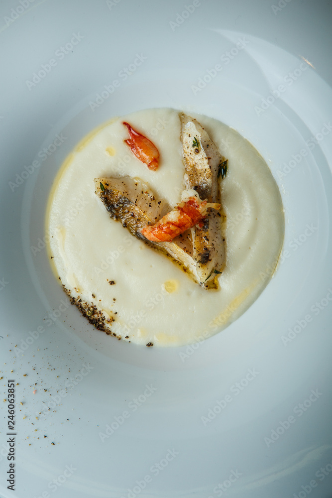 closeup fish cream soup decorated with fried pieces of fish, prawn, and spices