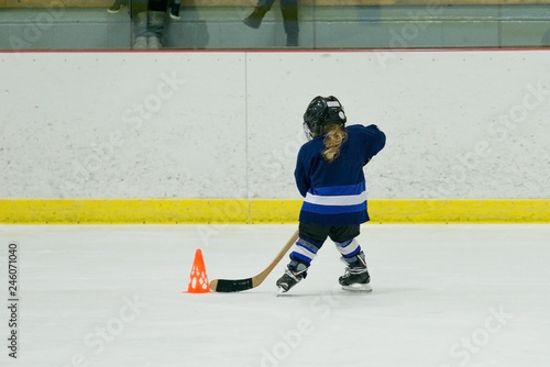 A Little girl in full hockey equipment is doing workouts on ice. Photo from the back. 