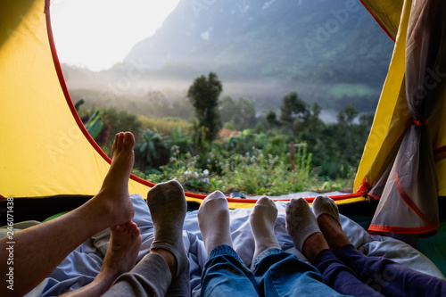 Close up foot of group of friends relax lying down and cross leg on blanket in tent and looking at mountain view in sunrise time at camping vacation holiday.