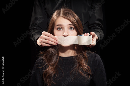 Man taped his mouth with a scotch tape to a young woman on a black background.