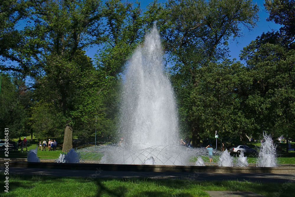 Obraz premium Water fountain with some people around on sunny Sunday afternoon