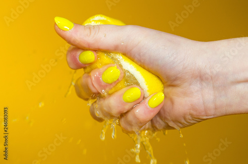 hand with yellow fingernails crushing a fresh, juicy lemon