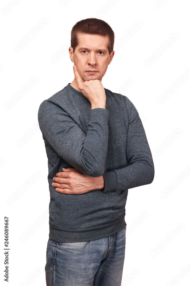 The thoughtful man is dressed in long sleeved t-shirt, jeans and holds a hand about a chin The thoughtful man is dressed in long sleeved t-shirt, jeans and holds a hand about a chin