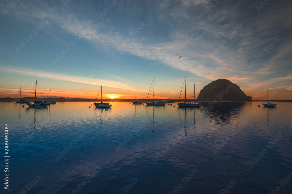 Beautiful sunset over the sea with sailing boats, rock, blue water, and amazing cloudy sky, Morro Bay harbor, California Beautiful sunset over the sea with sailing boats, rock, blue water, and amazing cloudy sky, Morro Bay harbor, California