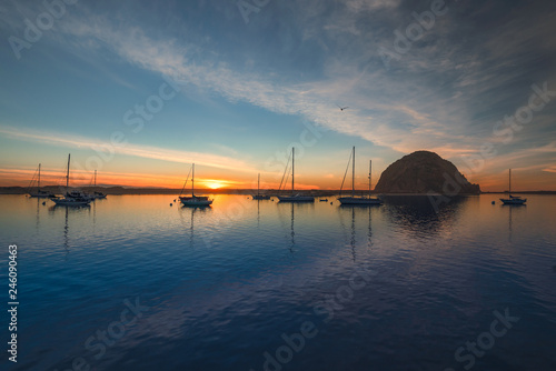 Beautiful sunset over the sea with sailing boats, rock, blue water, and amazing cloudy sky, Morro Bay harbor, California