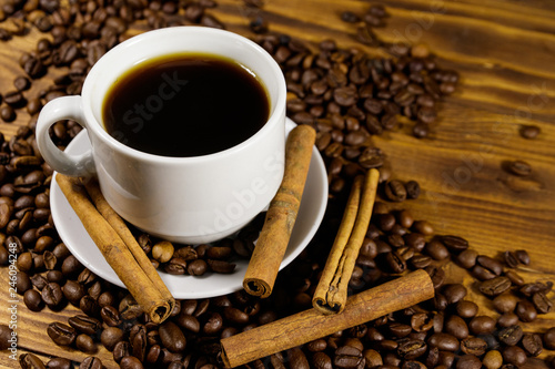 Cup of coffee, roasted coffee beans and cinnamon sticks on wooden table