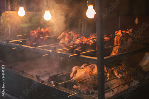 outdoor street chicken barbecue grill with broiler spit roasted over smoking living coals in a simple electric illumination, the Philippine lechon Manok