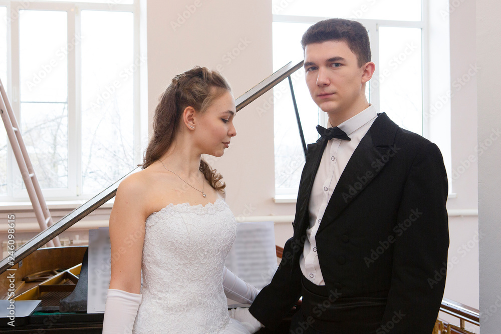 Young good looking couple in evening dress and dress coat posing in elegant way in a classical style Young good looking couple in evening dress and dress coat posing in elegant way in a classical style