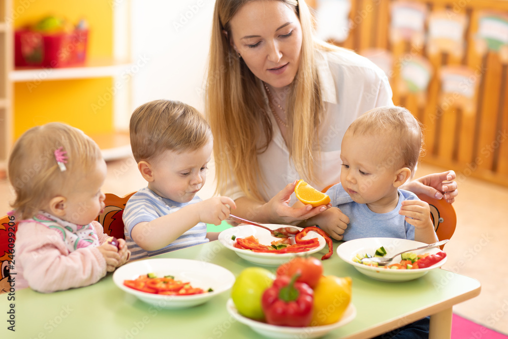 Lunch in nursery. Educator feeding babies in canteen Lunch in nursery. Educator feeding babies in canteen