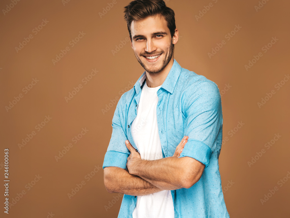 ortrait of handsome smiling stylish hipster lumbersexual businessman model dressed in blue shirt clothes. Fashion man posing on golden background.Crossed arms ortrait of handsome smiling stylish hipster lumbersexual businessman model dressed in blue shirt clothes. Fashion man posing on golden background.Crossed arms