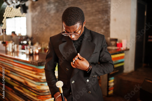 Stylish african american gentleman in elegant black jacket and glasses, holding retro walking stick as cane flask or tippling cane with golden diamond ball handle. Rich fashionable afro man. photo