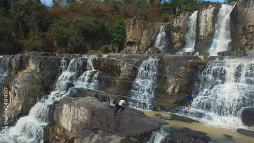 Aerial rotation across Dalat Pongour waterfalls as group of Vietnamese people climb over rocks. photo