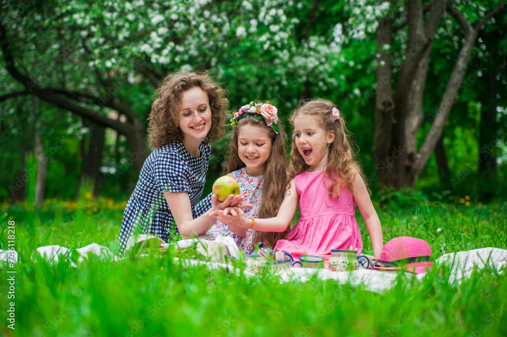 A family of three girls sitting on a blanket on the grass in blooming apple blossom garden.