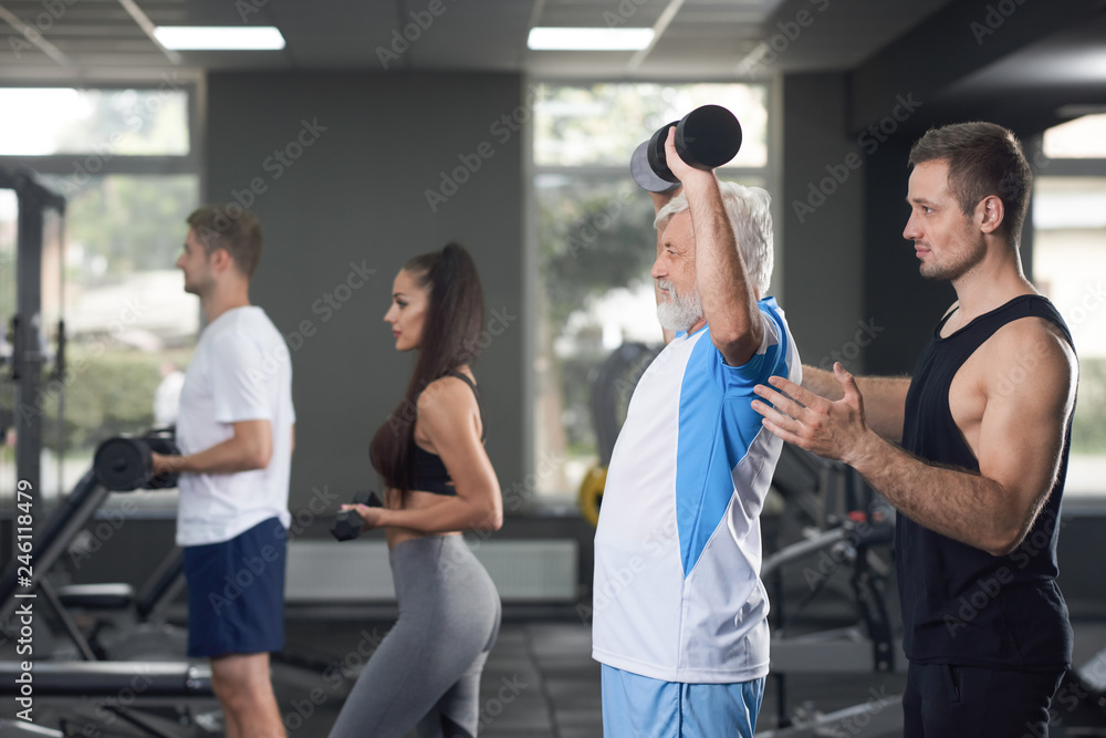 Elderler serious man training in crowded gym. - obrazy, fototapety, plakaty 
