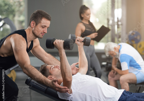 Trainer supporting man working out with dumbbells.