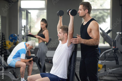 Fit man working out in gym with personal trainer. photo