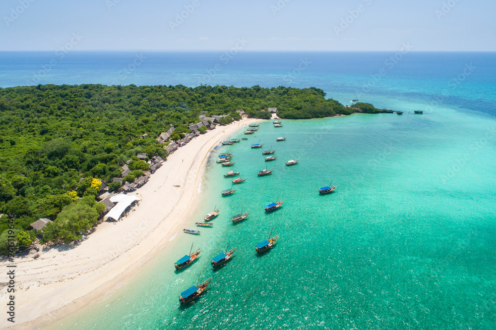 curved sand beach with boats in emerald water on tropical island on Zanzibar