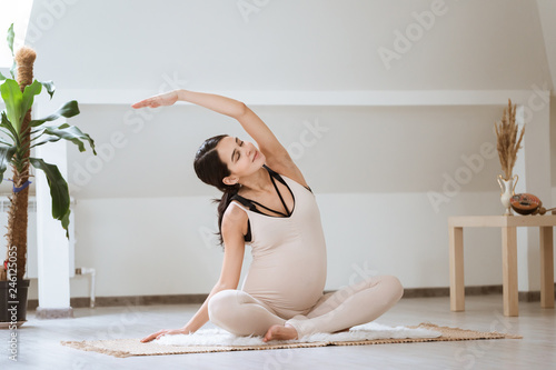 Pregnant woman stretching and training at home. Expectant female makes yoga exercise, healthy pregnancy concept