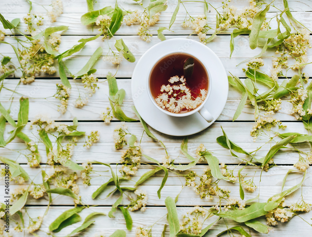 White cup of linden tea on linden blossom background. Herbal medicine. Top view. Treatment of cold and flu concept. White cup of linden tea on linden blossom background. Herbal medicine. Top view. Treatment of cold and flu concept.