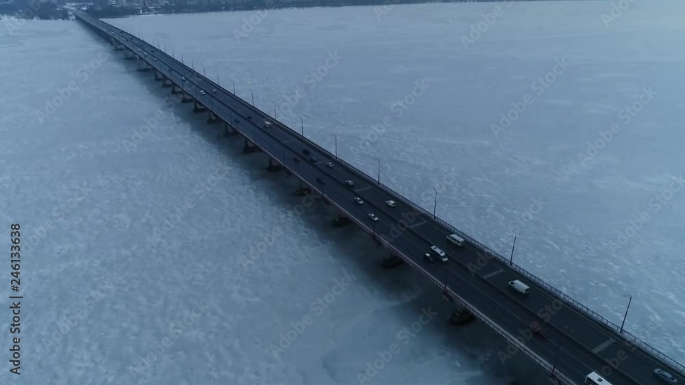 Aerial shot of the traffic on a bridge over a frozen white river Aerial shot of the traffic on a bridge over a frozen white river