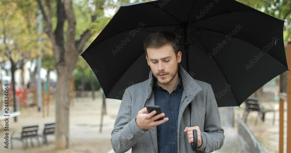 Disappointed man receiving wrong phone message in a rainy day walking in the street