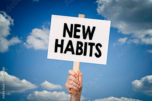 New habits message on board in hand with sky background