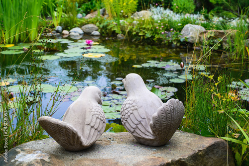A couple of birds - garden sculpture against a pond 
