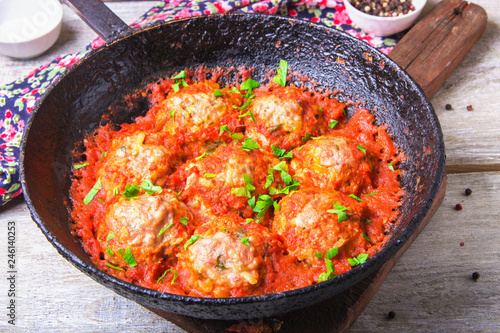 Meatballs in tomato sauce garlic and parsley in an iron frying pan on a white wooden background. Top view. Copy space