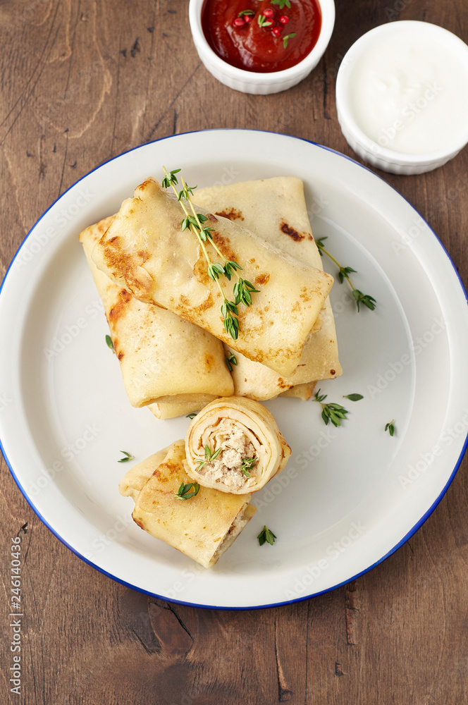Savory crepe rolls with ground meat filling served with sour cream and tomato sauce Savory crepe rolls with ground meat filling served with sour cream and tomato sauce