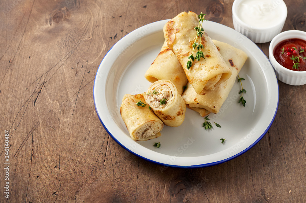 Savory crepe rolls with ground meat filling served with sour cream and tomato sauce Savory crepe rolls with ground meat filling served with sour cream and tomato sauce