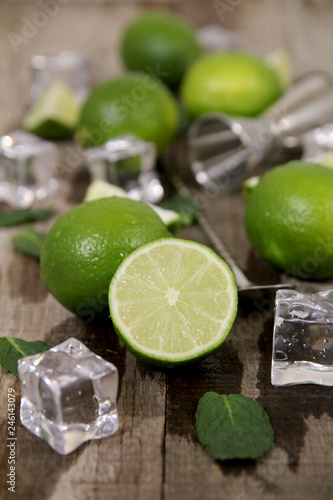 Ingredients for Mojito cocktail making. Bar utensils with cut and whole limes, mint and ice on wooden table