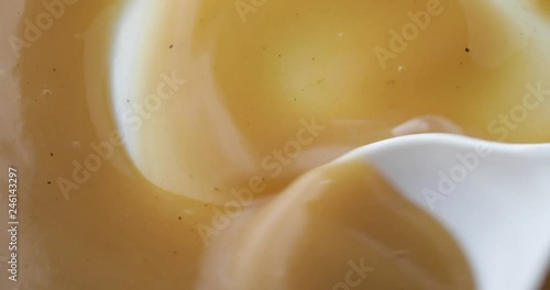 Close view of brown turkey gravy being stirred with a plastic spoon on a white plate.