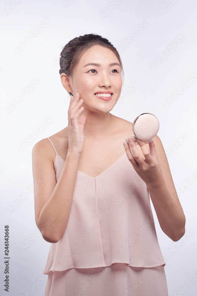 Young asian girl doing makeup, applying blusher to her cheek Young asian girl doing makeup, applying blusher to her cheek
